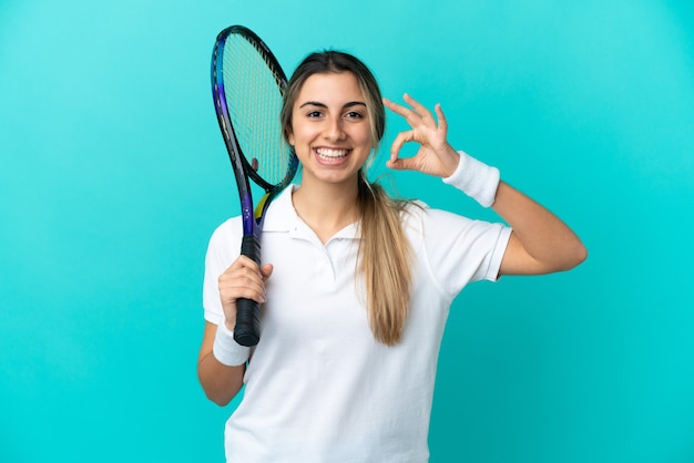 Tennisspielerin der jungen Frau lokalisiert auf blauem Hintergrund, der ok Zeichen mit den Fingern zeigt