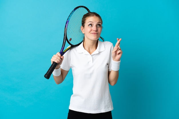 Tennisspielerin der jungen Frau lokalisiert auf blauem Hintergrund mit den Fingern, die kreuzen und das Beste wünschen