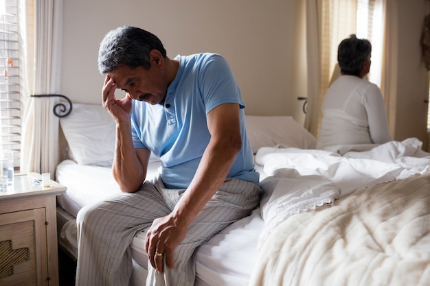 Tensado senior hombre sentado en la cama