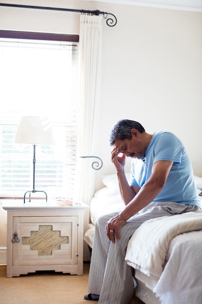 Tensado senior hombre sentado en la cama