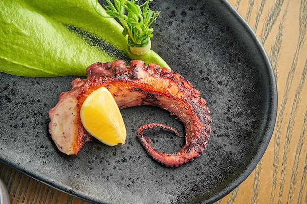 Tentáculo de polvo grelhado com smoothie verde e molho picante em uma placa preta em uma parede de madeira. Feche acima, foco seletivo