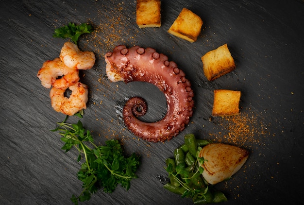 Tentáculo de pulpo a la plancha sobre placa de piedra negra con camarones