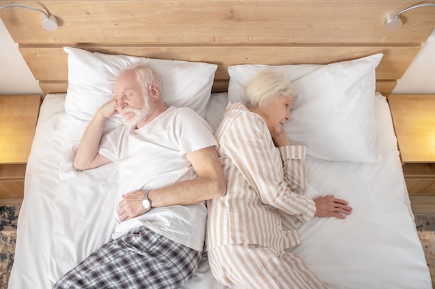 Tentando dormir. Casal idoso deitado na cama de costas