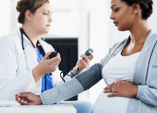 Tentando obter uma leitura foto recortada de uma médica confiante verificando a pressão arterial de uma paciente grávida em um hospital durante o dia