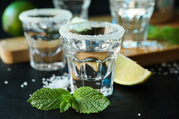 Tequila-Aufnahmen mit Salz, Limettenscheiben und Minze auf schwarzem Tisch