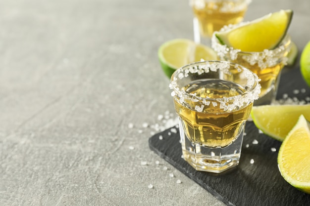 Tequila-Aufnahmen mit Salz- und Limettenscheiben auf Grau