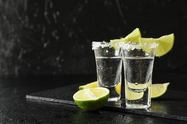 Tequila-Aufnahmen mit Salz- und Limettenscheiben auf schwarz nass