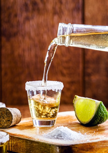 Tequila-Flasche, die ein Glas Getränk füllt Typisches mexikanisches Getränk wird serviert.