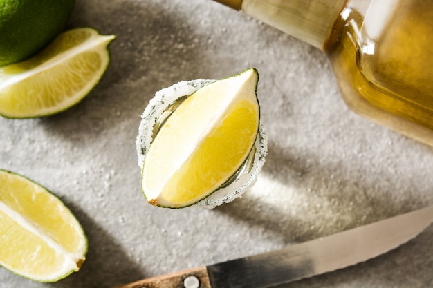 Tequila de oro mexicano con limón y sal sobre fondo gris vista superior