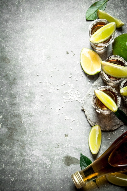 Foto tequila con sal y rodajas de lima. sobre la mesa de piedra.