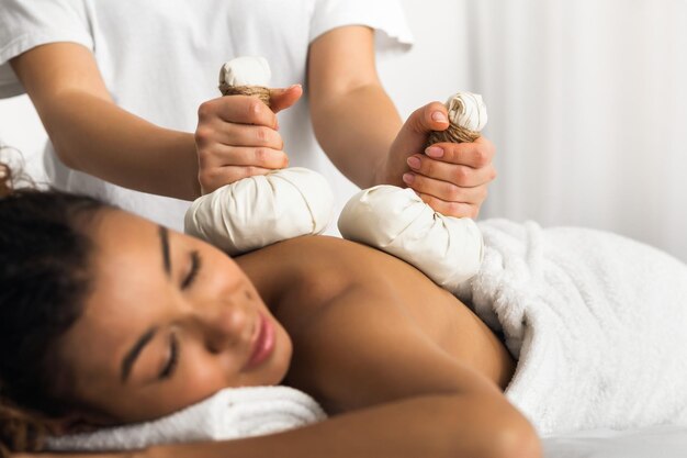 Foto terapeuta a aplicar compressas de ervas para uma senhora negra.