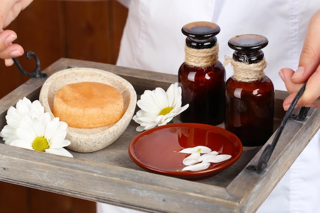 Terapeuta de belleza sosteniendo la bandeja de tratamientos de spa closeup sobre fondo de pared de madera