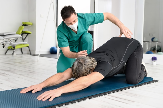 Terapeuta com máscara protetora facial auxiliando o paciente nos exercícios de alongamento.