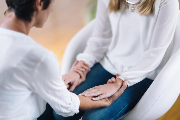 Terapeuta de curación Theta femenina realizando tratamiento de terapia alternativa con una paciente joven Terapeuta tomándose de la mano y transfiriendo energía Usando ropa blanca