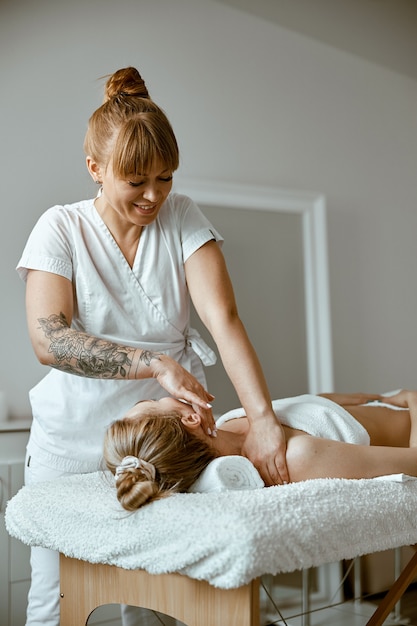 El terapeuta está haciendo un masaje relajante facial a una mujer joven en un moderno gabinete de bienestar.