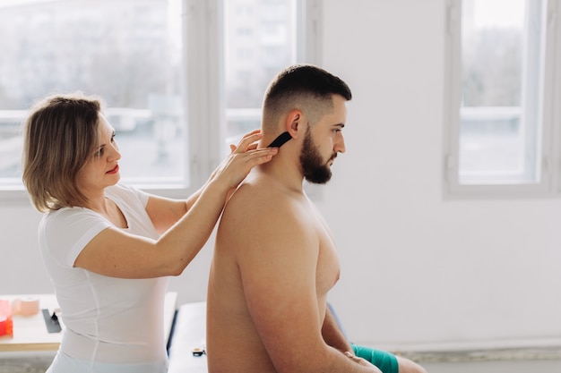 Un terapeuta grabando cinta de kinesiología en el cuello del paciente.