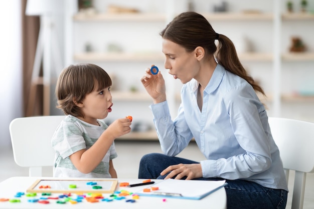 Terapeuta del habla femenina curando problemas e impedimentos de los niños niño pequeño aprendiendo la letra o con