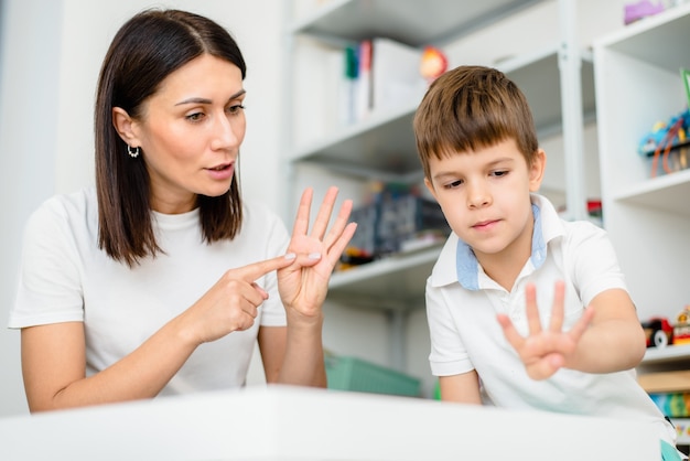 La terapeuta del habla hermosa mujer enseña al niño la pronunciación correcta de palabras y sonidos en la oficina