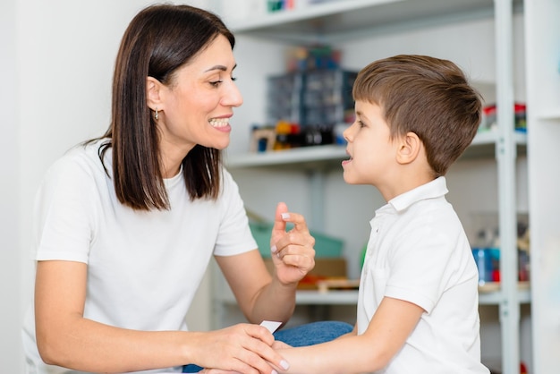 La terapeuta del habla hermosa mujer enseña al niño la pronunciación correcta de palabras y sonidos en la oficina