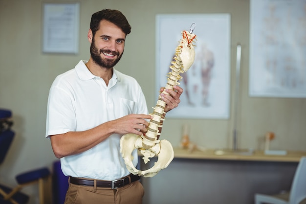 Terapeuta masculino con modelo de columna vertebral en clínica