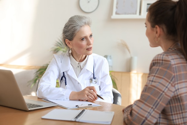 Terapeuta médica feminina de meia idade em consulta com o paciente no consultório.