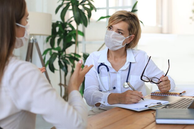 Terapeuta médica feminina de meia idade na máscara médica em consulta com o paciente no escritório.