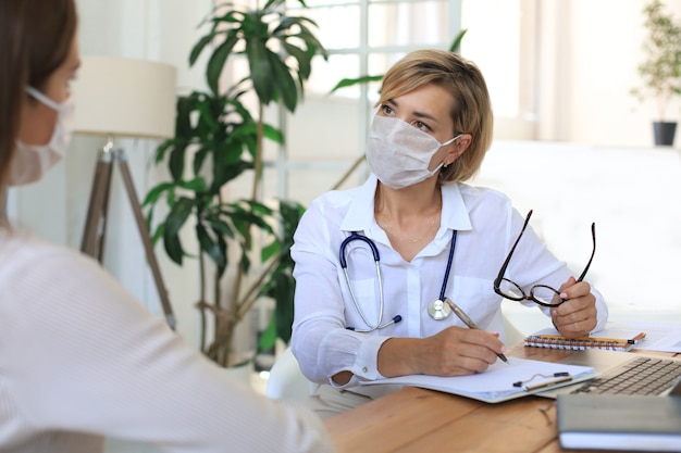 Terapeuta médico de mediana edad en máscara médica en consulta con el paciente en la oficina.