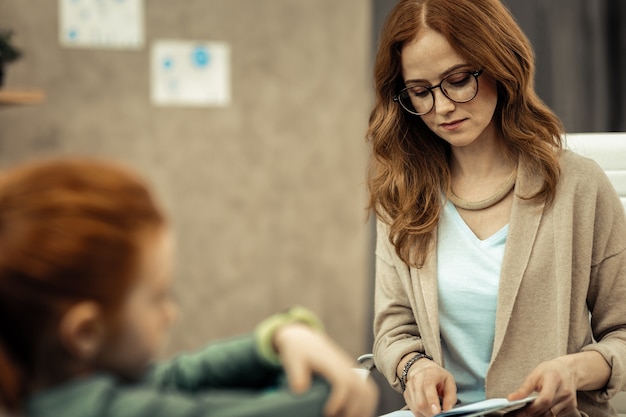 Terapeuta profesional. Grave mujer inteligente mirando sus notas mientras piensa en su paciente