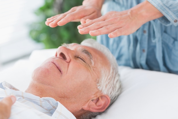 Terapeuta que realiza Reiki sobre hombre mayor