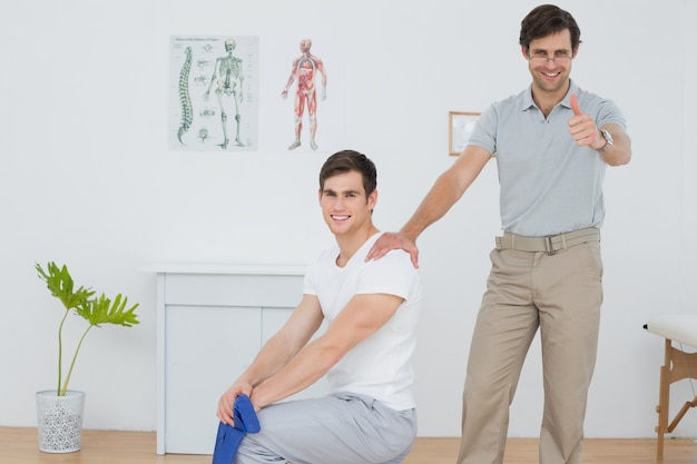 Foto terapeuta sonriente que gesticula los pulgares para arriba con el hombre joven