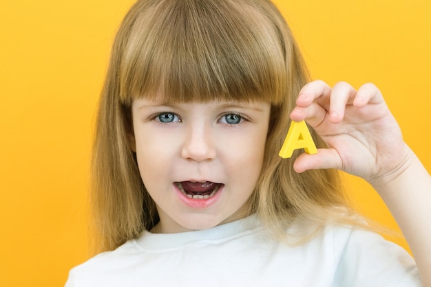 Foto terapia da fala garota da criança segurando a letra a em suas mãos aulas com uma fonoaudióloga garota em fundo amarelo isolado