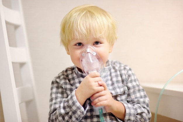 Terapia de inalação de menino bonito pela máscara de inalador. Feche acima da imagem de uma criança com problema respiratório ou asma. Menino doente com máscara de oxigênio clara.