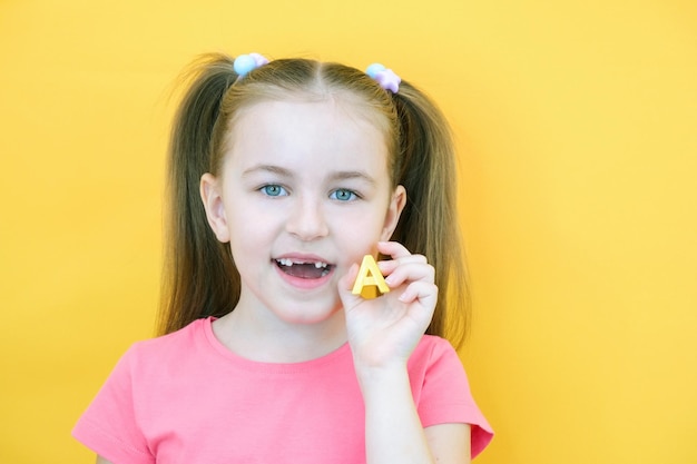 Terapia del habla Niña pequeña sosteniendo la letra A en sus manos Clases con un terapeuta del habla Niña sobre fondo amarillo aislado