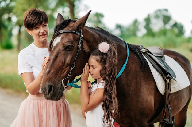 Terapia infantil para pasear a caballo. Contacto emocional con el caballo. Pasear a madre e hija en el verano en el parque con un caballo.