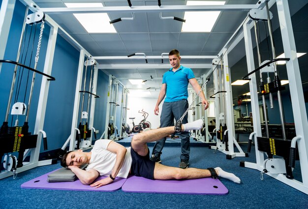 Terapia de rehabilitación. Hombre joven que hace ejercicios en la estera bajo supervisión del fisioterapeuta.