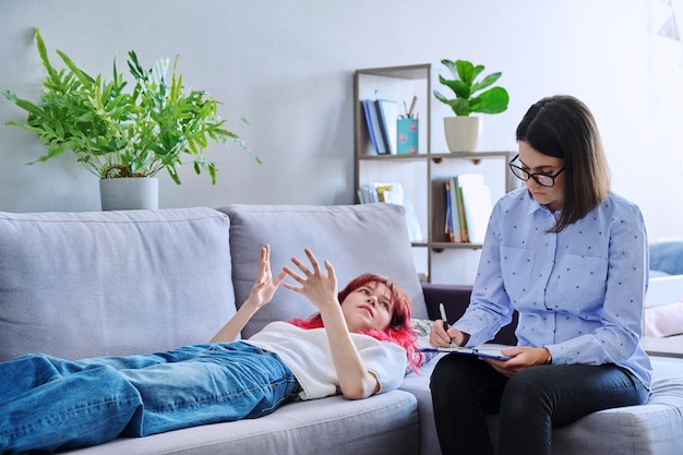 Foto terapia de sesión de una estudiante adolescente con un psicólogo de consejería adolescente acostada en el sofá hablando sobre problemas de salud mental terapia de psicología de la adolescencia psicoterapia ayuda profesional