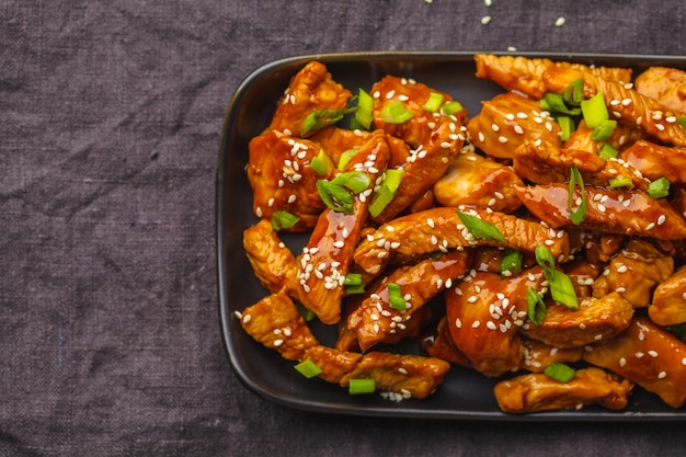 Teriyaki-Huhn mit indischem Sesam, Frühlingszwiebel im Schwarzblech, dunkler Hintergrund.