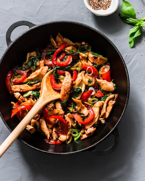 Teriyaki-Huhn, Paprika, Zwiebeln und Spinat braten in einer Pfanne auf grauem Hintergrund, Draufsicht