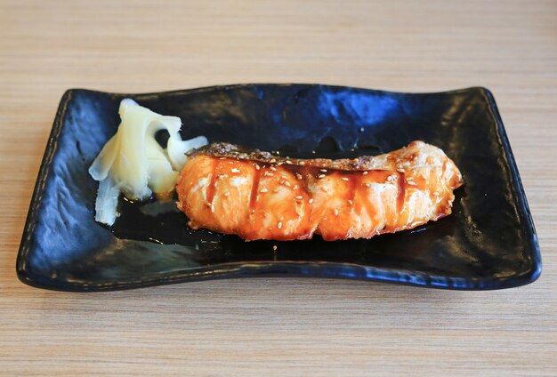 Teriyaki Salmon na placa preta na tabela de madeira, alimento japonês.