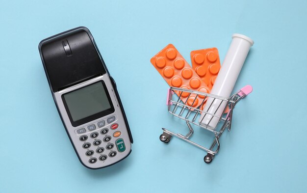 Terminal de pagamento e carrinho de compras com comprimidos blister em fundo azul brilhante Compra de medicamentos Vista superior