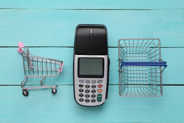 Terminal de pago y cesta de supermercado y carro sobre fondo de madera azul Pago por compras