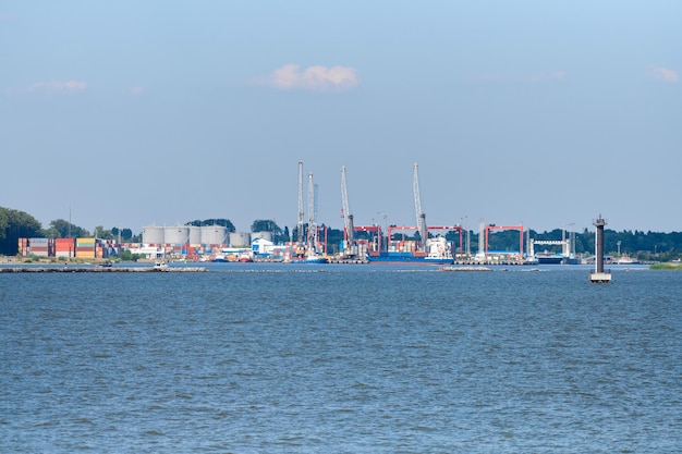 Terminal de portacontenedores en logística de exportación e importación. Envío de carga al puerto por grúa, cielo azul y mar, día. Transporte de carga, envío mundial, logística, comunicaciones globales, industria