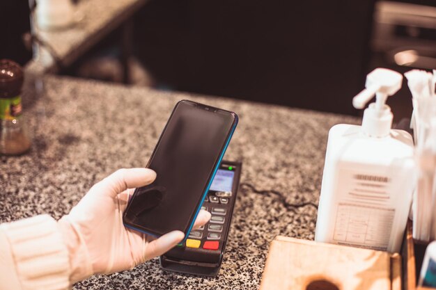 Foto terminal pos no balcão do café ou restaurante método de pagamento sem contato para manter o distanciamento social durante a pandemia closeup mãos da mulher em luvas de proteção segurando cartão bancário perto do terminal pos