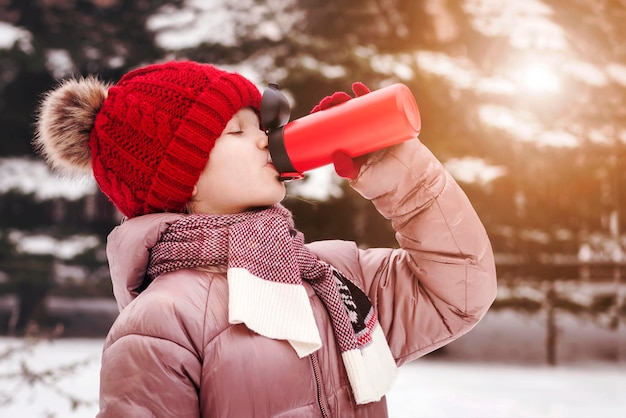 Termo para crianças. Menina bebendo bebida quente da caneca térmica em Cold Snow Winter Park.