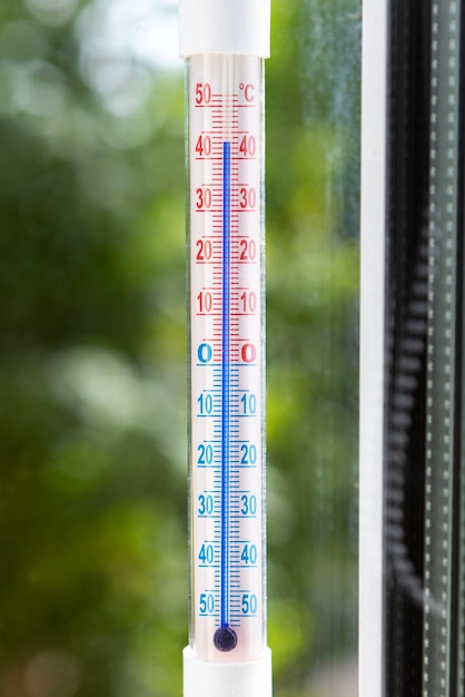 Un termómetro Celsius en el marco de una ventana muestra altas temperaturas durante las olas de calor fuera Foto conceptual del clima cálido