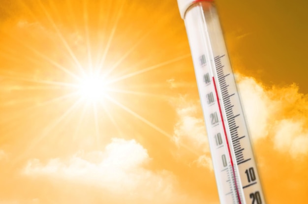 Termómetro contra el fondo de un resplandor amarillo anaranjado de nubes y sol, concepto de clima cálido.