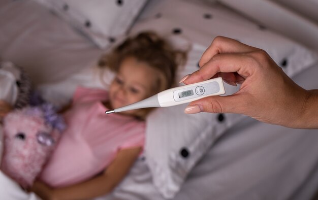 El termómetro electrónico muestra una temperatura alta en el contexto de un niño enfermo en la cama