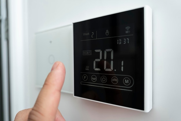 Foto termómetro electrónico de temperatura confortable en la habitación de 20 grados celsius en la pared primer plano de una mano masculina caucásica que ajusta el termostato digital montado en la pared moderno