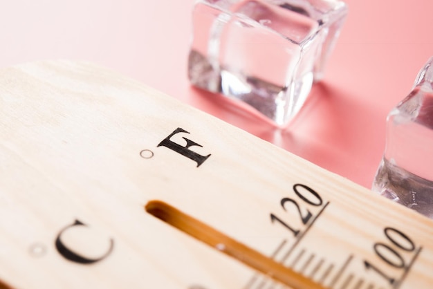 El termómetro de madera muestra altas temperaturas en grados Fahrenheit o Celsius sobre fondo rosa claro con hielo