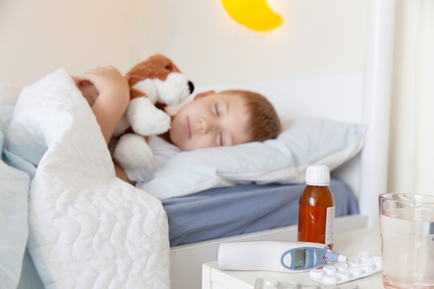 Termómetro, medicina y un vaso de agua sobre la mesa cerca del niño enfermo durmiendo bo